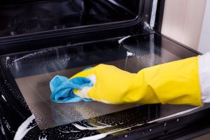 Close up of hand with yellow protective gloves cleaning oven door glass