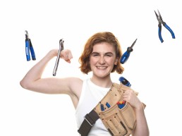 A young woman smiling and flexing her right bicep while surrounded by tools